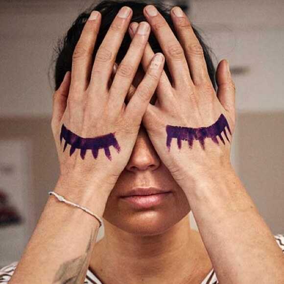 Fotografi: En mamma håller båda händerna för ansiktet. På händerna är två stängda ögonlock målade.