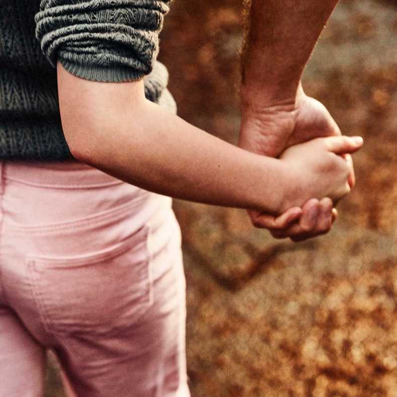 Fotografi: Ett barn som håller en vuxen i handen.