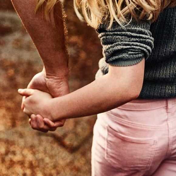 Fotografi: En närbild två händer. Det är en dotter och en pappa som håller händerna då de är ute och promenerar.