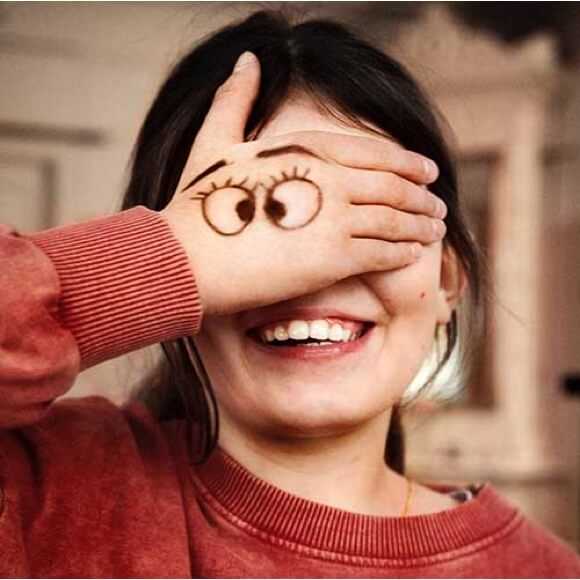 Fotografi: En glad flicka i 10-årsåldern håller handen framför ansiktet. På handen har hon målat ett par roliga ögon som ser i kors.